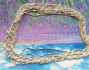 May include: A pile of silver chain necklaces with a box chain design. The chains are arranged in a circle on a floral background.