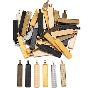 May include: A collection of rectangular pendant trays in various metallic finishes, including gold, silver, black, and bronze. The trays have a textured surface and a loop at the top for attaching to a chain or cord. The pendants are suitable for jewelry making.