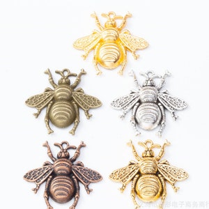 May include: Five bee charms in different finishes: gold, silver, bronze, and two shades of gold. The bee charms have detailed wings and a textured body.