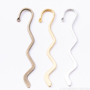May include: Three metal bookmark designs with a wavy shape. The bookmarks are in bronze, gold, and silver.