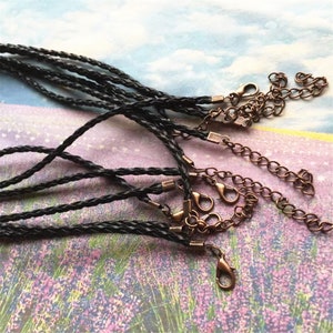 Op de afbeelding: Een set van tien zwarte gevlochten leren koorden met karabijnhaken. De koorden zijn ongeveer 45 cm lang en perfect voor het maken van kettingen, armbanden of sleutelhangers.
