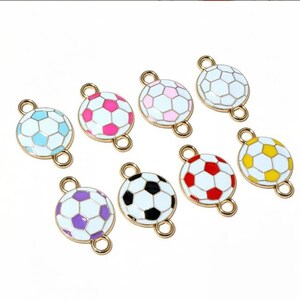 May include: A selection of football-shaped charms in a range of colours: blue, pink, white, red, yellow, black, and purple. Each charm has a gold-coloured loop for attaching to jewellery or other crafts.