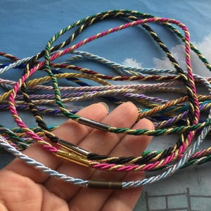 May include: A collection of colorful twisted cords, featuring a variety of colors including green, pink, gold, and blue. Each cord has a metallic clasp. The cords are approximately 18 inches in length.
