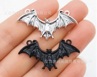 May include: Two silver-tone bat charms, one black and one silver, with a loop for hanging. The charms are in the shape of a bat with wings spread out.