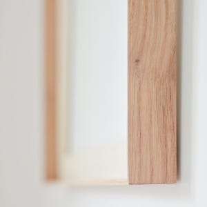 May include: Close-up of a wooden frame with visible wood grain, set against a white background. The frame is a light brown color and appears to be part of a larger structure. The image is well-lit, highlighting the texture of the wood.