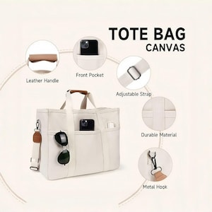 Può includere: Borsa tote in tela color crema con più tasche, un manico in pelle e una tracolla regolabile. La borsa presenta la scritta "TOTE BAG CANVAS". Occhiali da sole e uno smartphone sono visibili nelle tasche. La borsa ha un gancio in metallo.