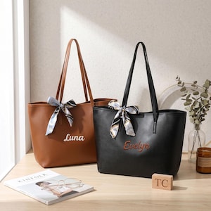 May include: Two tote bags, one brown and one black, each featuring two shoulder straps and a decorative patterned scarf tied to the handle. The brown bag has the name Luna embroidered in white, and the black bag has the name Evelyn embroidered in orange.