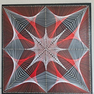 May include: A square string art piece featuring a geometric star pattern created with red and white thread wrapped around silver nails on a black board. The design consists of intersecting lines forming a complex, symmetrical, multi-pointed star.