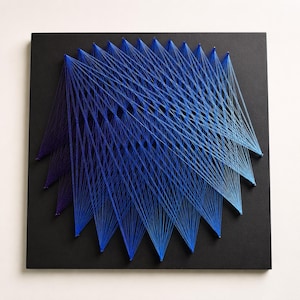 May include: A square black board featuring a geometric string art design created with blue thread. The thread is wrapped around small nails to form a series of overlapping, fan-like patterns that transition from deep purple-blue to light cyan.
