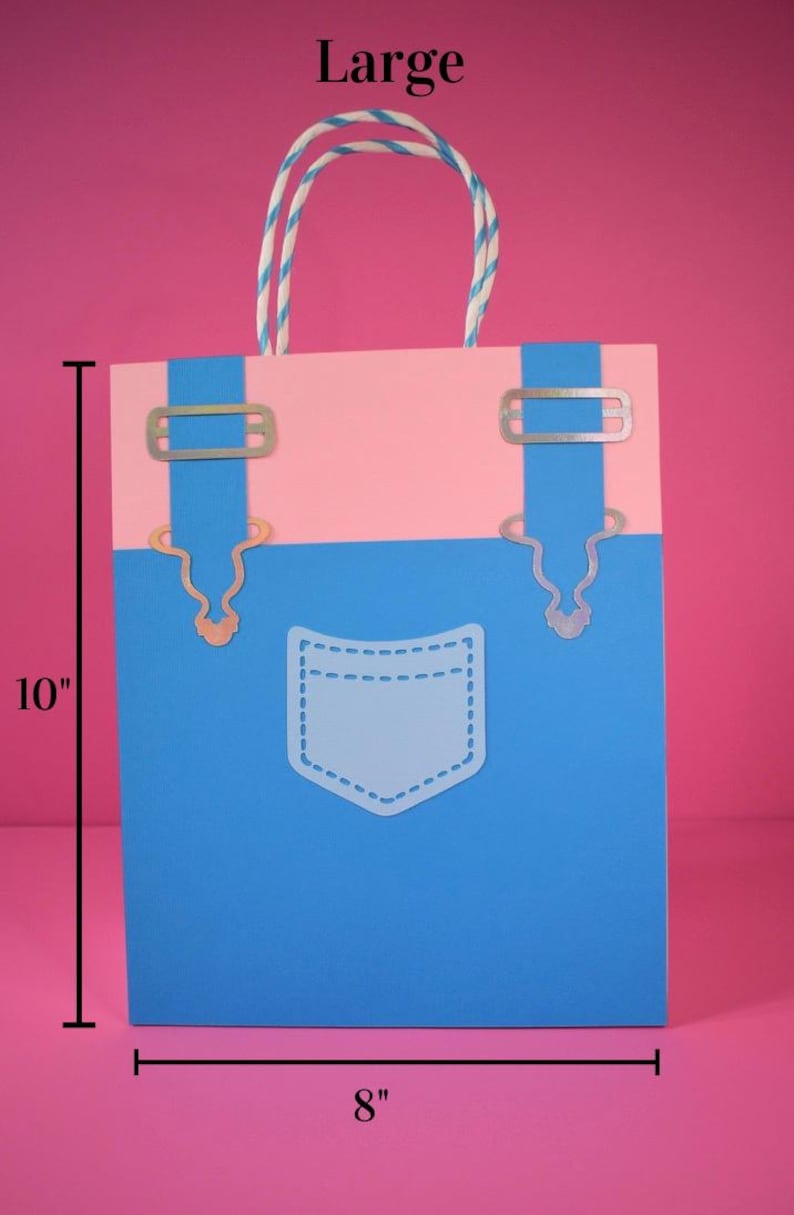 May include: A large gift bag with a blue and pink design, resembling denim overalls. The bag is 10 inches tall and 8 inches wide, with a white pocket outline and silver-colored metal accents. The handle is a twisted white and blue cord.