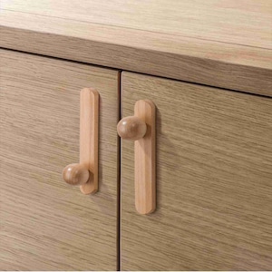 May include: Close-up of a wooden cabinet with two doors. Each door has a vertical wooden handle with a rounded knob. The cabinet and handles are made of light-colored wood, showcasing a natural grain pattern.