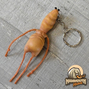 May include: A quirky, orange-hued keychain with a distinctive creature design. The keychain has a rounded body, a segmented head, and orange string-like appendages. It includes a silver keyring and chain.