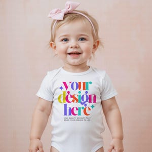 May include: A smiling baby wearing a white onesie with the text "YOUR design here" in colorful letters. The onesie also has the text "HIGH QUALITY MOCKUPS THAT BRING YOUR DESIGNS TO LIFE". The baby is wearing a pink headband with a bow.