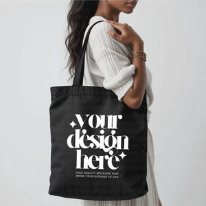 May include: A black tote bag with white text that reads "YOUR design HERE". The bag also has the text "HIGH QUALITY MOCKUPS THAT BRING YOUR DESIGNS TO LIFE". The bag is held by a person.