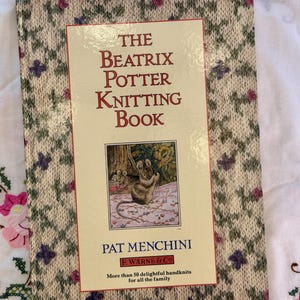 May include: A copy of "The Beatrix Potter Knitting Book" by Pat Menchini. The book's cover has a cream background with a floral design and a central image of a mouse knitting. It promises over 50 delightful handknits for the family.