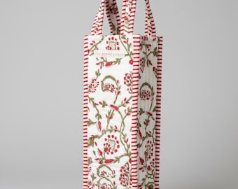 May include: A white quilted wine tote with a red and green floral pattern. The tote has red striped trim and handles. The text "THE BOMBAY BAZAAR" is printed on the front.