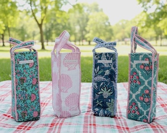 May include: Four tall, rectangular fabric wine bags with handles, each featuring distinct block-print patterns in teal, pink, and navy blue. Each bag has a small white rectangular label with black text and pink striped trim.
