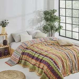 Puede incluir: Una colcha colorida y estampada con diseños geométricos y tribales cubre una cama. La colcha presenta rayas de color naranja, verde, morado y rosa. La cama está en una habitación luminosa con una ventana grande y cojines decorativos.