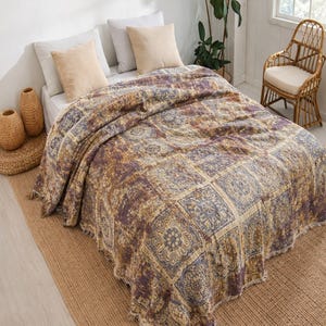 Peut inclure: Un couvre-lit présentant un motif carré répétitif dans des tons de violet sourd, d'or et de crème. Le tissu a un aspect texturé avec un bord à franges effilochées sur le bas. Le design se compose de motifs floraux et géométriques complexes.