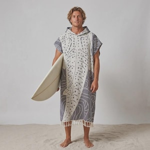 Könnte beinhalten: Ein Kapuzen-Poncho-Handtuch mit einem abstrakten Walhai-Muster in Dunkelanthrazit und Off-White. Das Kleidungsstück hat eine lockere, ärmellose Passform mit Kapuze und einen geraden Saum, der am unteren Rand mit dekorativen Fransen versehen ist.