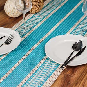 May include: A dining table set with a turquoise and white patterned runner. White plates with black cutlery are arranged on the table. Wine glasses and decorative items complete the elegant setup.