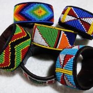 Puede incluir: Una colección de pulseras con cuentas en varios diseños y colores. Las pulseras presentan intrincados patrones con cuentas en tonos rojos, verdes, amarillos, azules y blancos. Las pulseras están hechas de cuero y cuentas.