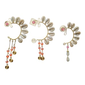 May include: Three gold-toned ear cuffs, each featuring a crescent of white seashells. The cuffs are adorned with pink beads and dangling accents. The design includes spiral and geometric shapes, creating a unique, bohemian aesthetic.