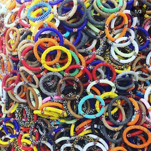 May include: A vibrant collection of beaded bracelets in various colors, including red, blue, yellow, and orange. The bracelets are tightly woven with small beads, creating a textured surface. The bracelets are stacked together, showcasing a variety of designs.