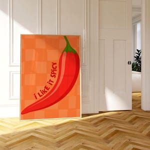 May include: A framed art print showing a large red chilli pepper with a green stem against an orange checkered background. The text "I like it spicy" is written vertically on the left side of the pepper.