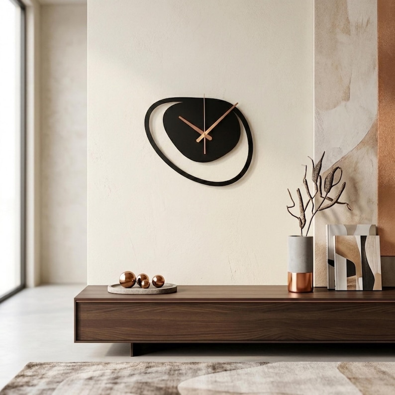 Pu&ograve; includere: Un moderno orologio da parete nero con un design astratto unico. L'orologio presenta una forma ovale nera con un cerchio interno nero pi&ugrave; piccolo e lancette color rame. Montato su una parete color crema, sopra un mobile in legno scuro. Misura circa 40 cm di diametro.