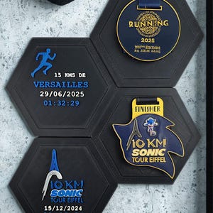 Peut inclure: Ensemble de tuiles hexagonales noires avec des médailles de course. Les médailles bleues et dorées affichent des inscriptions telles que "10 KM Sonic Tour Eiffel" et "15 KMS DE VERSAILLES", avec des dates et des heures.