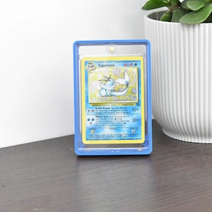 May include: A Vaporeon Pokémon trading card in a blue protective case. The card features a blue and white illustration of Vaporeon, with text including "Vaporeon" and "80 HP". The card is set against a light background.