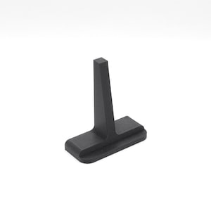 Op de afbeelding: Een matzwart, T-vormig object met een rechthoekige basis en een verticale paal. Het object is gemaakt van een massief materiaal en staat tegen een witte achtergrond. Het ontwerp is minimalistisch en modern.