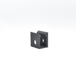 May include: A dark gray metal bracket with a U-shaped design. The bracket has two holes and a small lip on one side. The object is set against a white background.