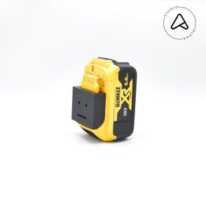 May include: A yellow and black DeWalt 18V XR 5.0Ah Li-Ion battery with a black adapter. The battery has a rectangular shape and is designed for power tools. The adapter has a simple, blocky design.