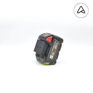 May include: Black and red M18 5.0 REDLITHIUM-ION battery pack with a black adapter. The battery pack has a yellow base and is slightly dirty. The image is set against a white background.