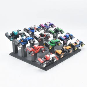 Op de afbeelding: Een verzameling miniatuur raceauto's in verschillende kleuren, waaronder rood, blauw, groen en oranje, tentoongesteld op een zwarte, gelaagde standaard. Elke auto heeft een uniek ontwerp en is ongeveer 7.6 cm lang.