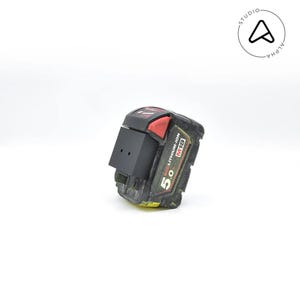 May include: A black and red M18 5.0 REDLITHIUM-ION battery pack for power tools. The battery pack has a black housing with red accents and a yellow base. The battery pack is slightly dirty.