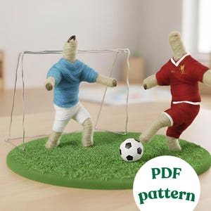 Peut inclure: Une scène de football artisanale avec deux figurines en fil de couleur bleu et rouge, jouant sur un terrain vert avec un ballon de football et un but en fil de fer. L'image comprend un cercle blanc avec le texte "PDF pattern".