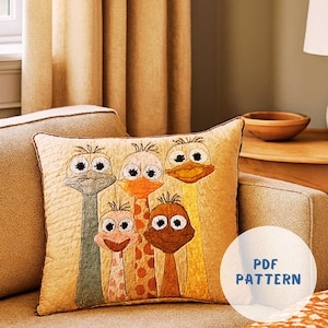 May include: A decorative square pillow featuring a whimsical design of five giraffe-like creatures with large eyes and long necks. The pillow has a quilted texture and is in shades of beige, orange, and brown. The text "PDF PATTERN" is visible on the image.