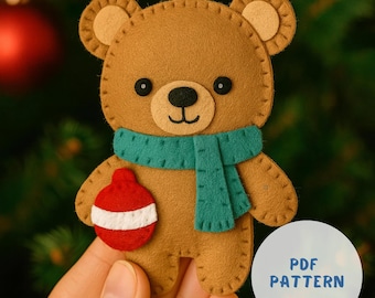 May include: A brown felt teddy bear Christmas ornament with a green scarf and a red and white ornament. The bear has black eyes and a black nose. The ornament is held by a white string. The text "PDF PATTERN" is on a white circle.