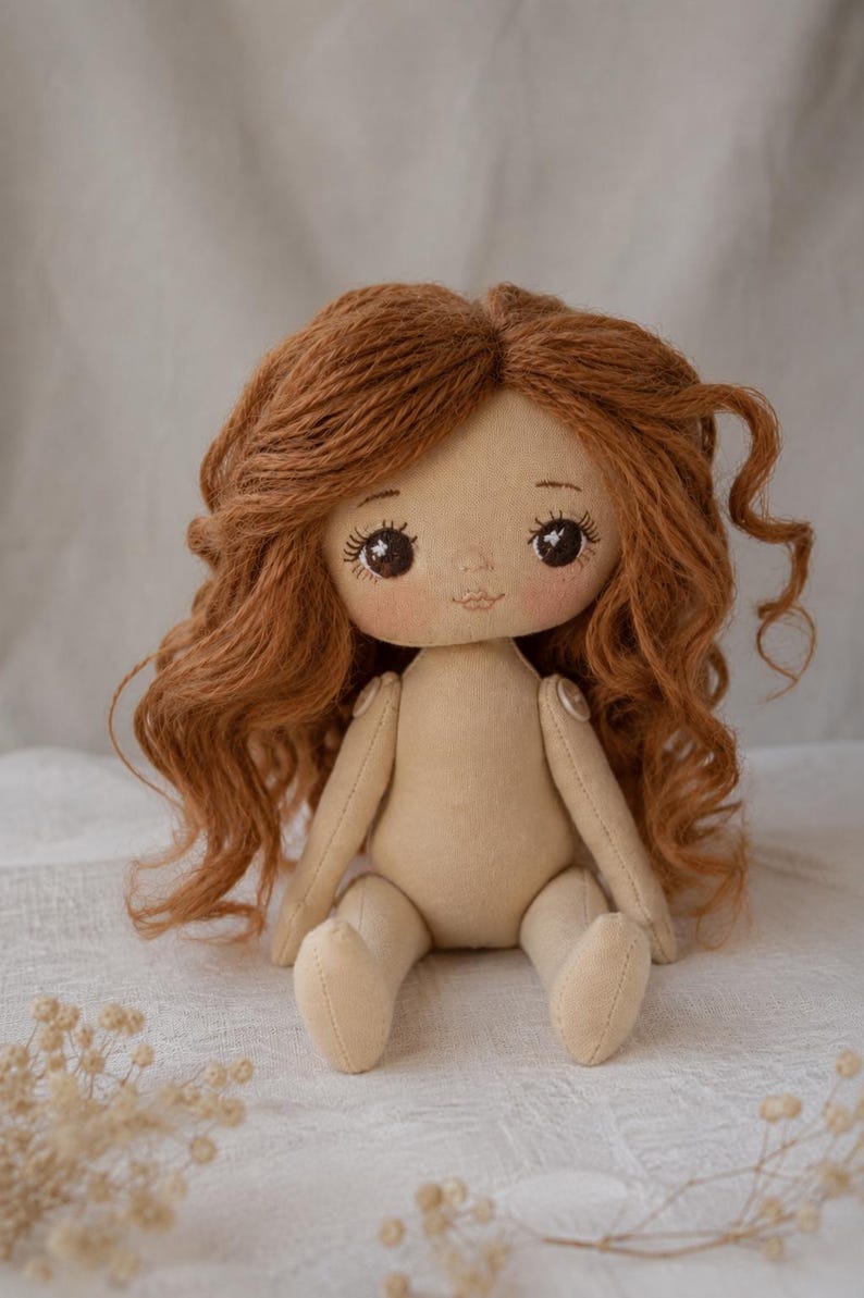 May include: A handmade fabric doll with light beige skin and long, wavy auburn yarn hair. The doll features embroidered facial details, including dark brown eyes with long lashes and a small mouth. The arms are attached with visible round buttons.