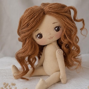 May include: A handmade fabric doll with long, wavy auburn yarn hair, dark brown embroidered eyes with long lashes, and a small stitched mouth. The doll has a light beige cloth body with a visible button joint at the shoulder and sits upright.