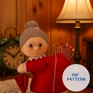 Può includere: Bambola in feltro fatta a mano raffigurante una nonna, con un vestito rosso con bordi in pizzo, occhiali e uno chignon grigio. La bambola tiene un piccolo ombrello rosso e ha un cuore a cuscinetto con spilli colorati. Il testo "PDF PATTERN" è incluso.