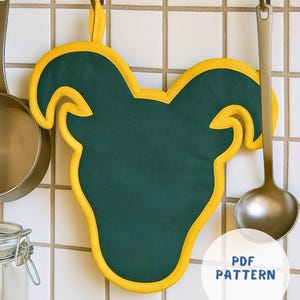 May include: A green and yellow ram-shaped pot holder hanging on a hook. The pot holder has a dark green center with a yellow outline and a loop for hanging. The text "PDF PATTERN" is in a white circle.