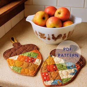 May include: Two acorn-shaped quilted pot holders with a patchwork design in shades of orange, green, and brown. A bowl of red and yellow apples sits nearby. The pot holders have a loop for hanging. The text "PDF PATTERN" is visible.