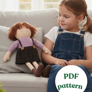Op de afbeelding: Een handgemaakte pop met bruin haar, een lavendelkleurig shirt en een geruite rok. De pop heeft bruine schoenen en zit op een grijze bank. De tekst "PDF pattern" is zichtbaar in de afbeelding.