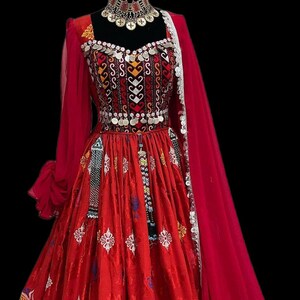 Op de afbeelding: Een levendige rode jurk met ingewikkelde borduursels en versieringen. De jurk heeft een vierkante halslijn, lange mouwen en een zwierige rok. Een bijpassende rode sjaal en een sierlijke ketting maken de outfit compleet. De jurk wordt op een mannequin gepresenteerd.