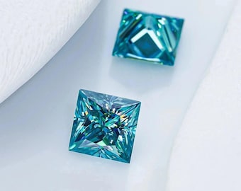 Könnte beinhalten: Zwei quadratisch geschliffene, teal-farbene Edelsteine mit aufwendigen Facetten werden vor einem weißen Hintergrund gezeigt. Die Edelsteine haben einen Prinzessinnenschliff, der das Licht reflektiert und einen funkelnden Effekt erzeugt. Das Thema ist Schmuck und Edelsteine.