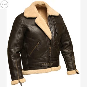 May include: A dark brown leather jacket with a cream-colored shearling collar and lining. The jacket features a zip-up front, multiple pockets, and a buckled belt at the waist. The sleeves have zippers at the cuffs.